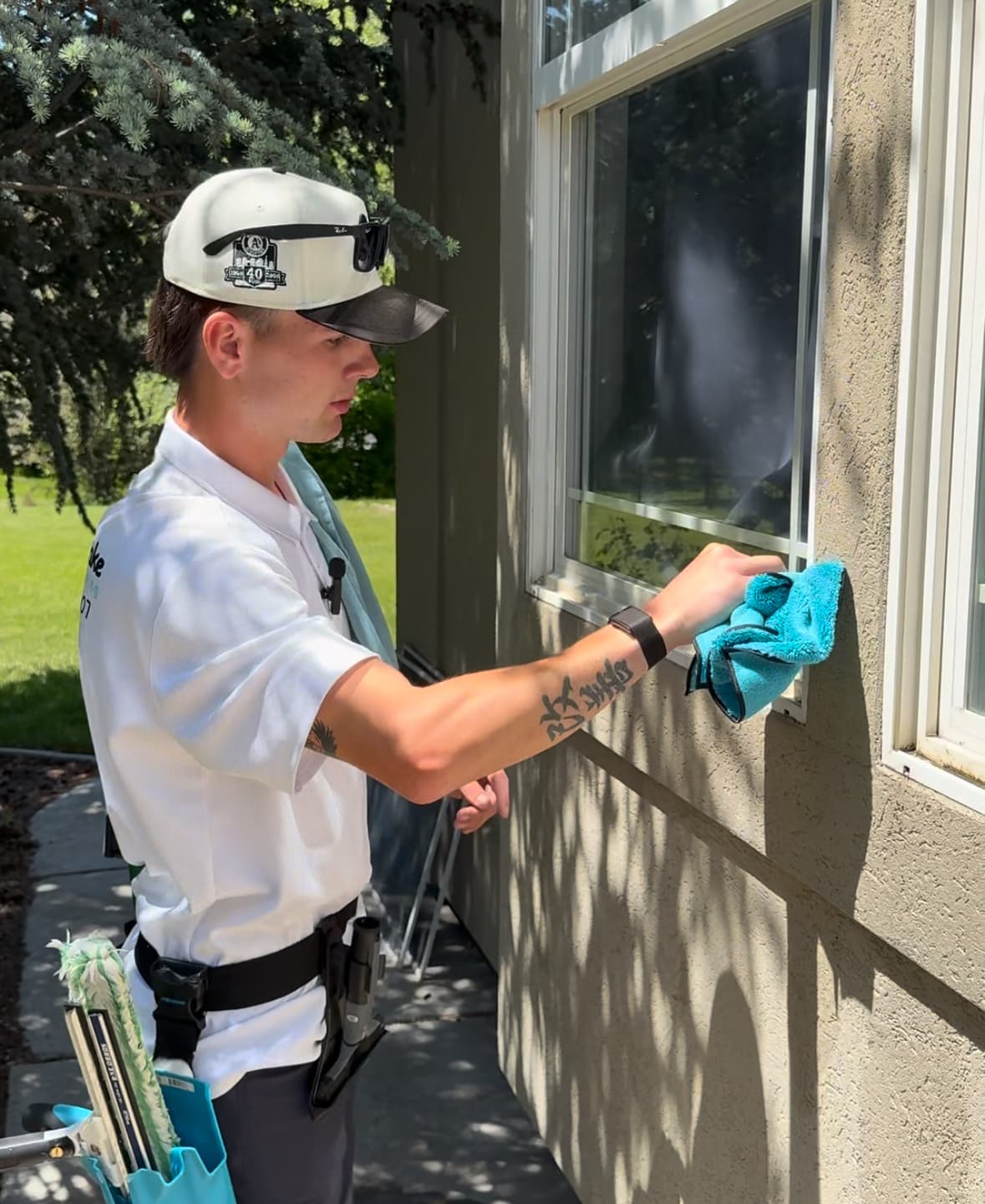 Professional window cleaner wipes an exterior window frame using a blue microfiber cloth.